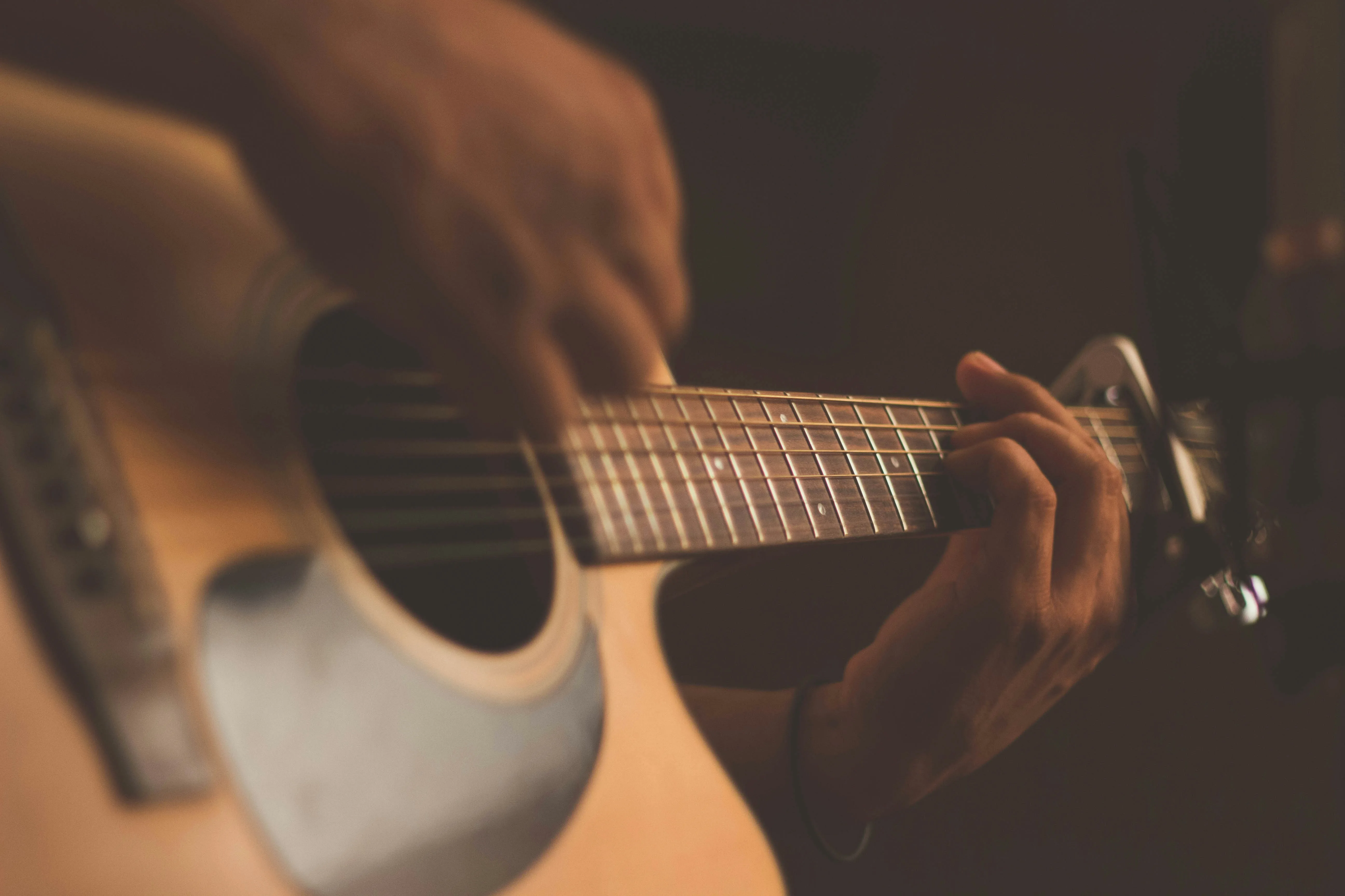 Hands playing acoustic guitar — learning through performance, not just practice