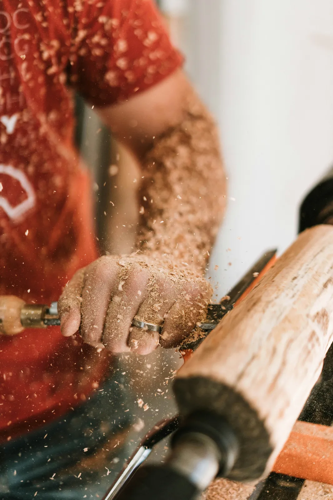 A builder shaping a piece of wood on a lathe, sawdust flying — the hands-on craft behind every boutique S-style guitar