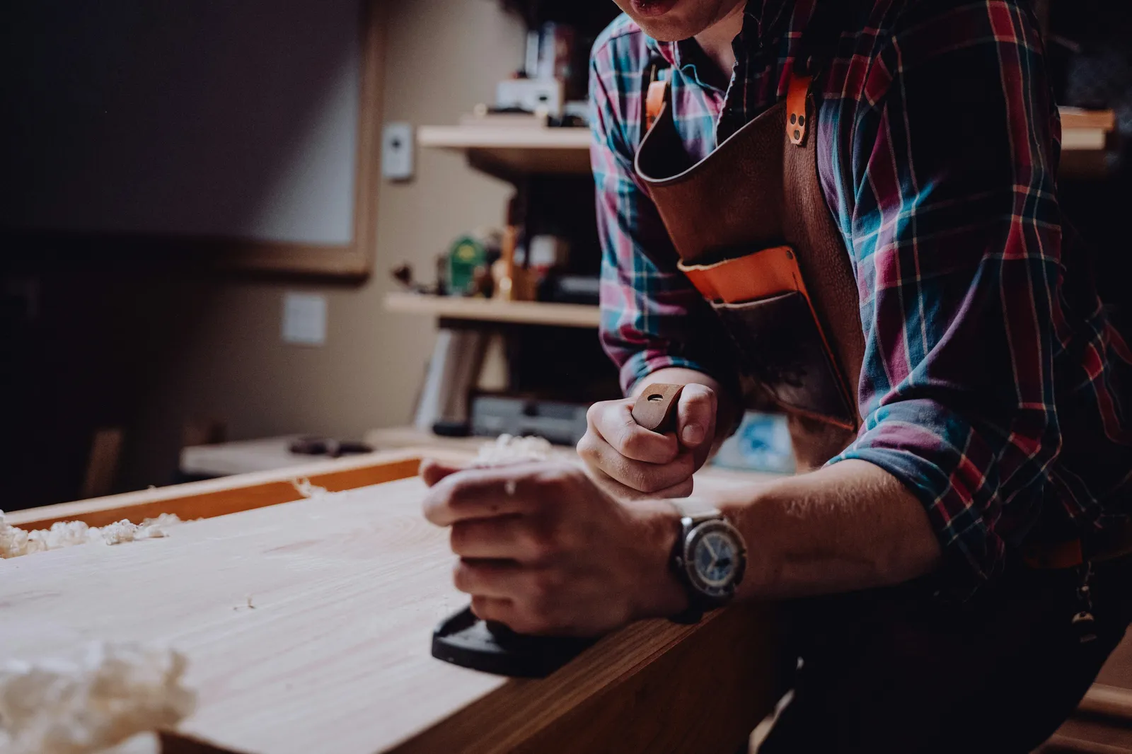 A craftsman planing a guitar body blank by hand at a boutique guitar shop workbench