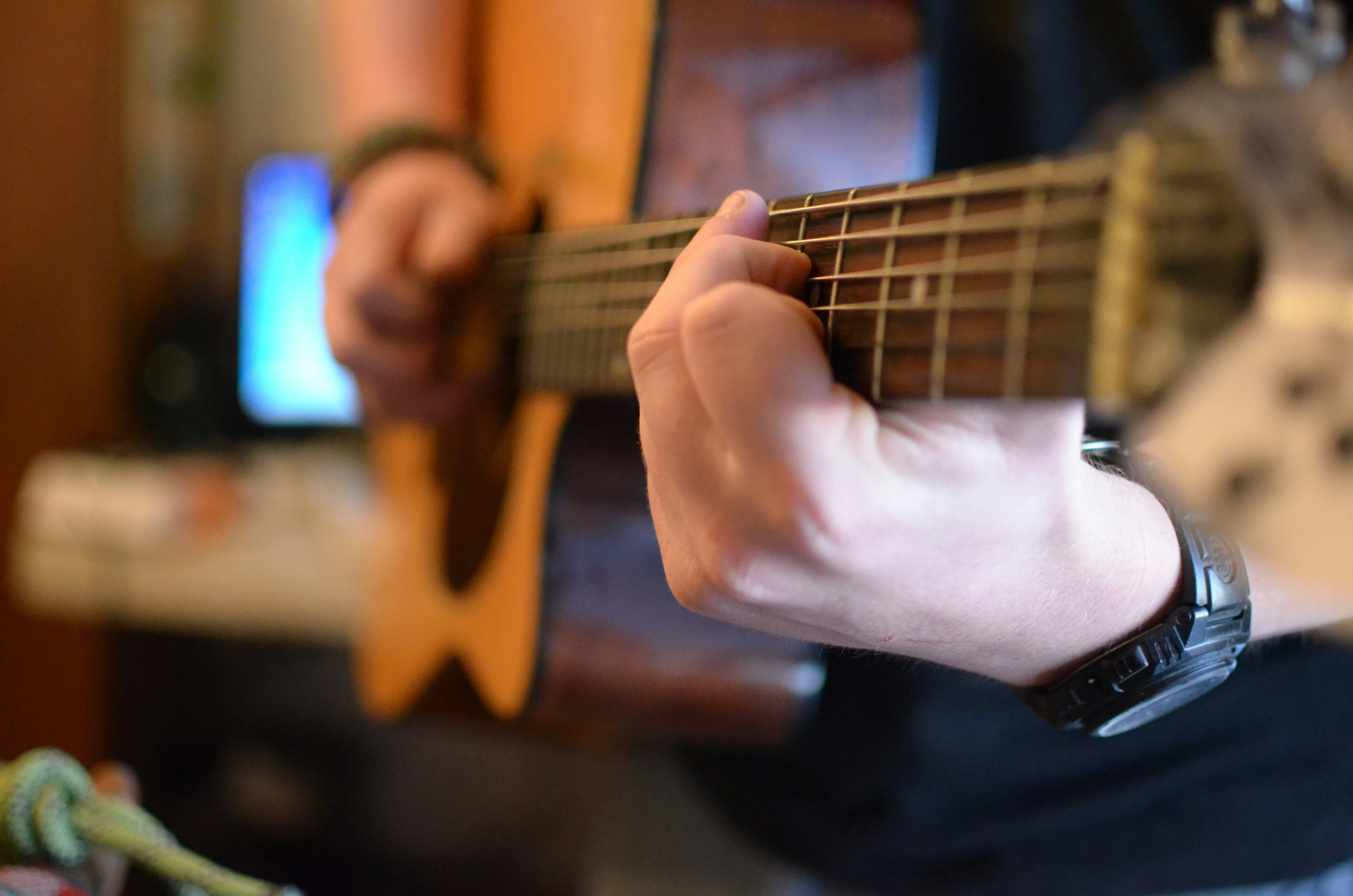 Close-up of a guitarist's fretting hand on the neck with a wristwatch on the wrist — balancing guitar practice with a full work schedule