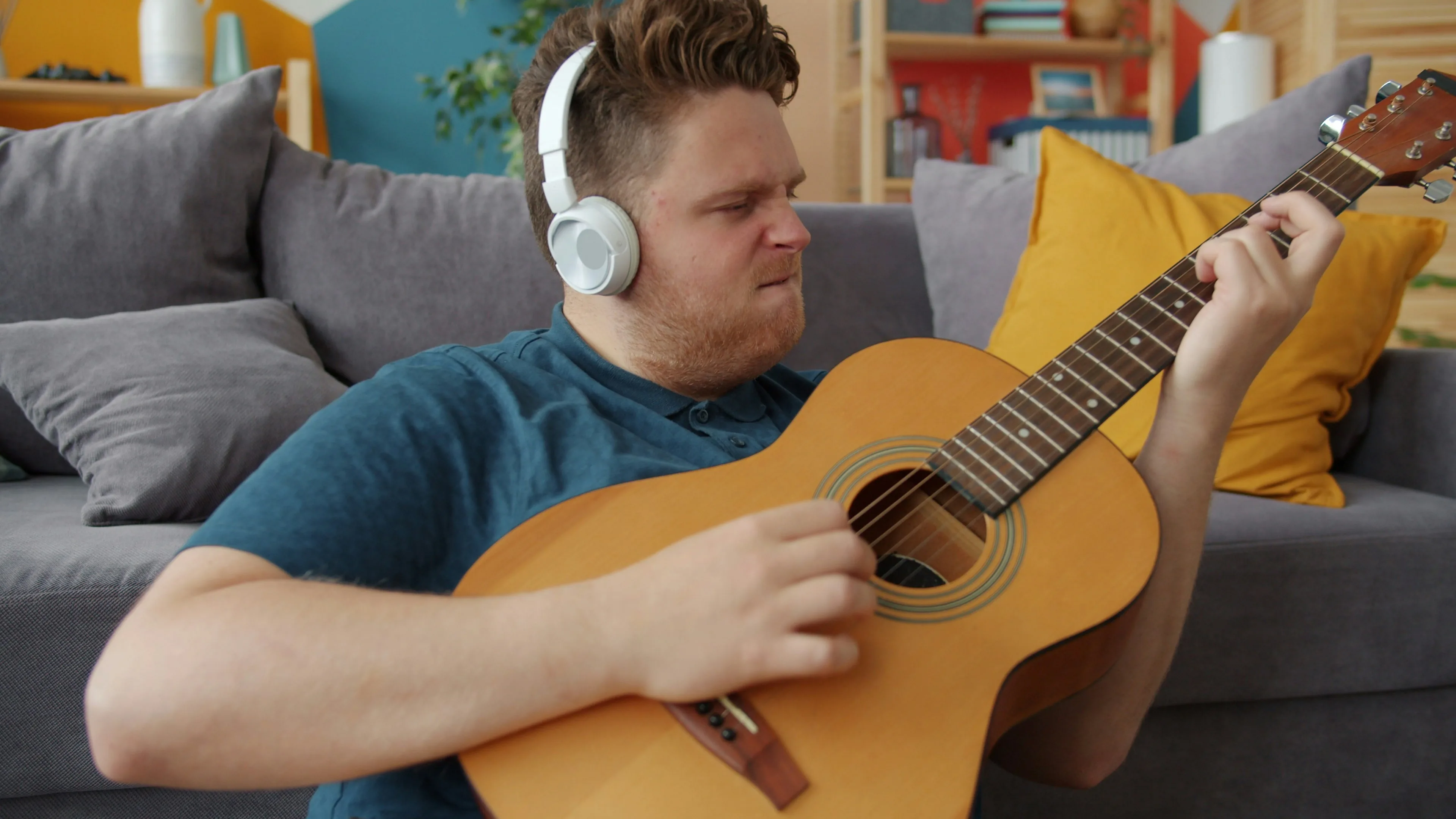 A guitarist wearing headphones plays acoustic guitar on the couch at home — using practice time to decompress after a long workday