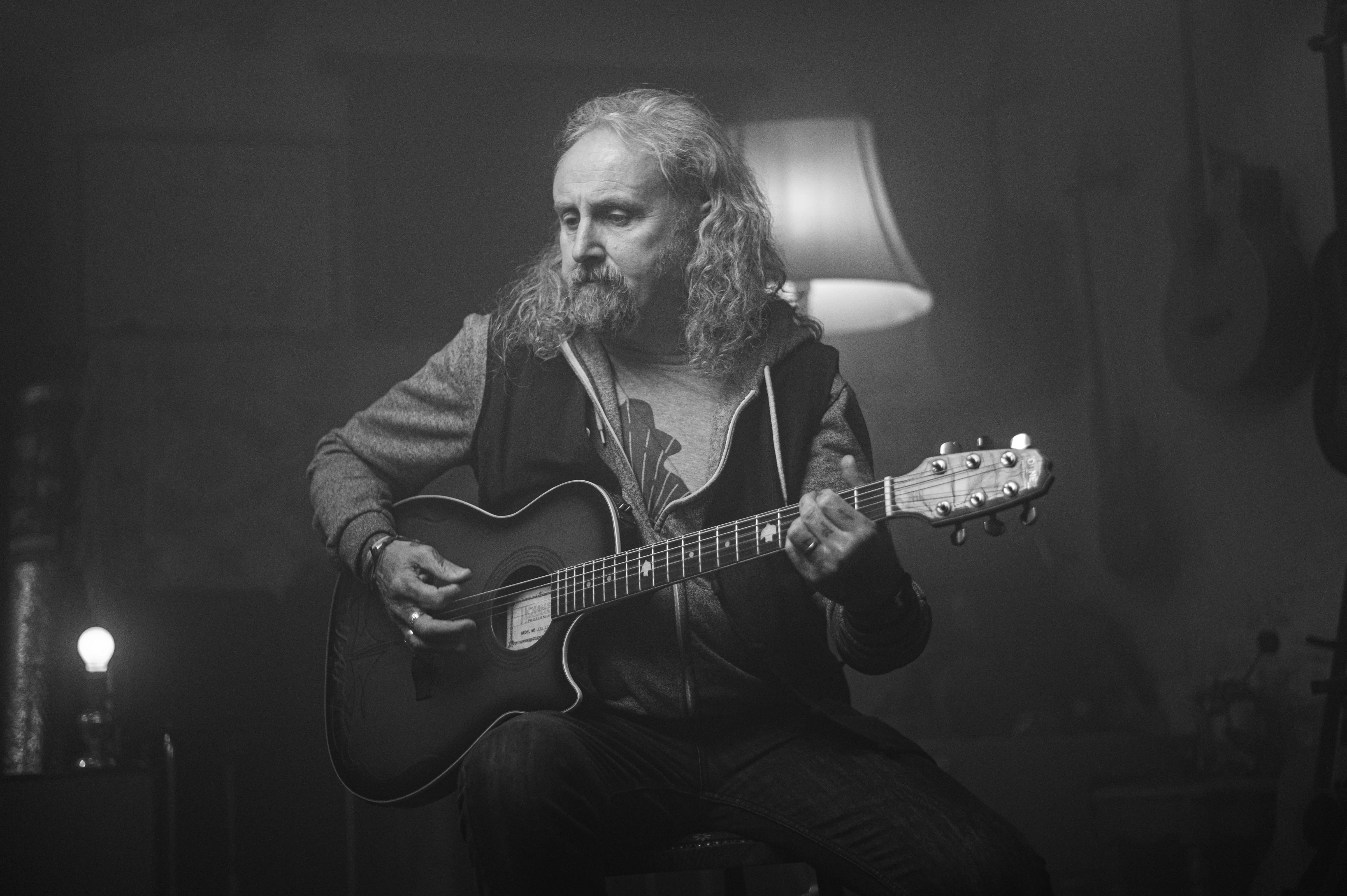 Adult guitarist practicing acoustic guitar at home in a lamp-lit room