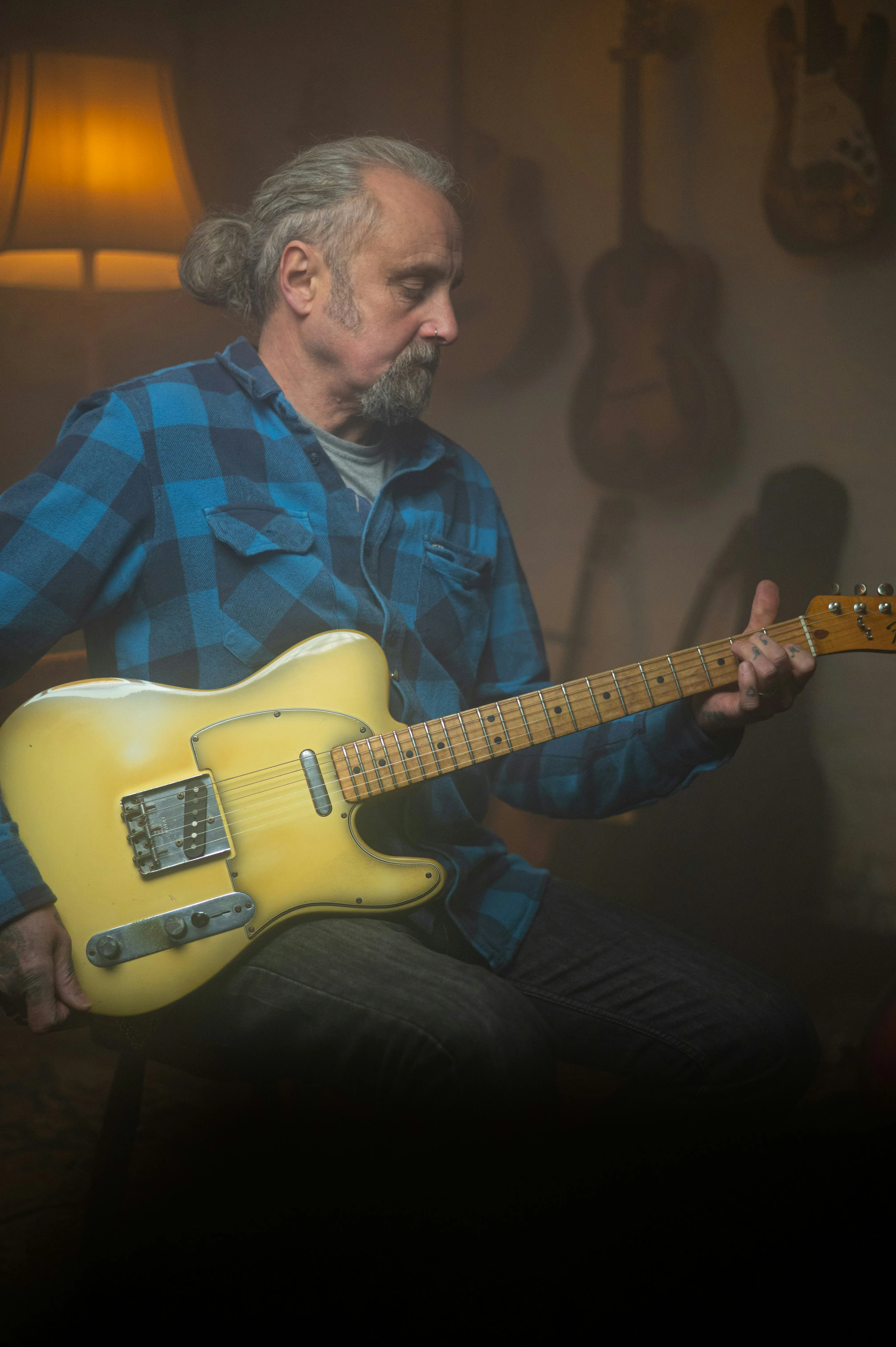 Older adult guitarist playing a Telecaster in a warm lamp-lit room — learning guitar later in life