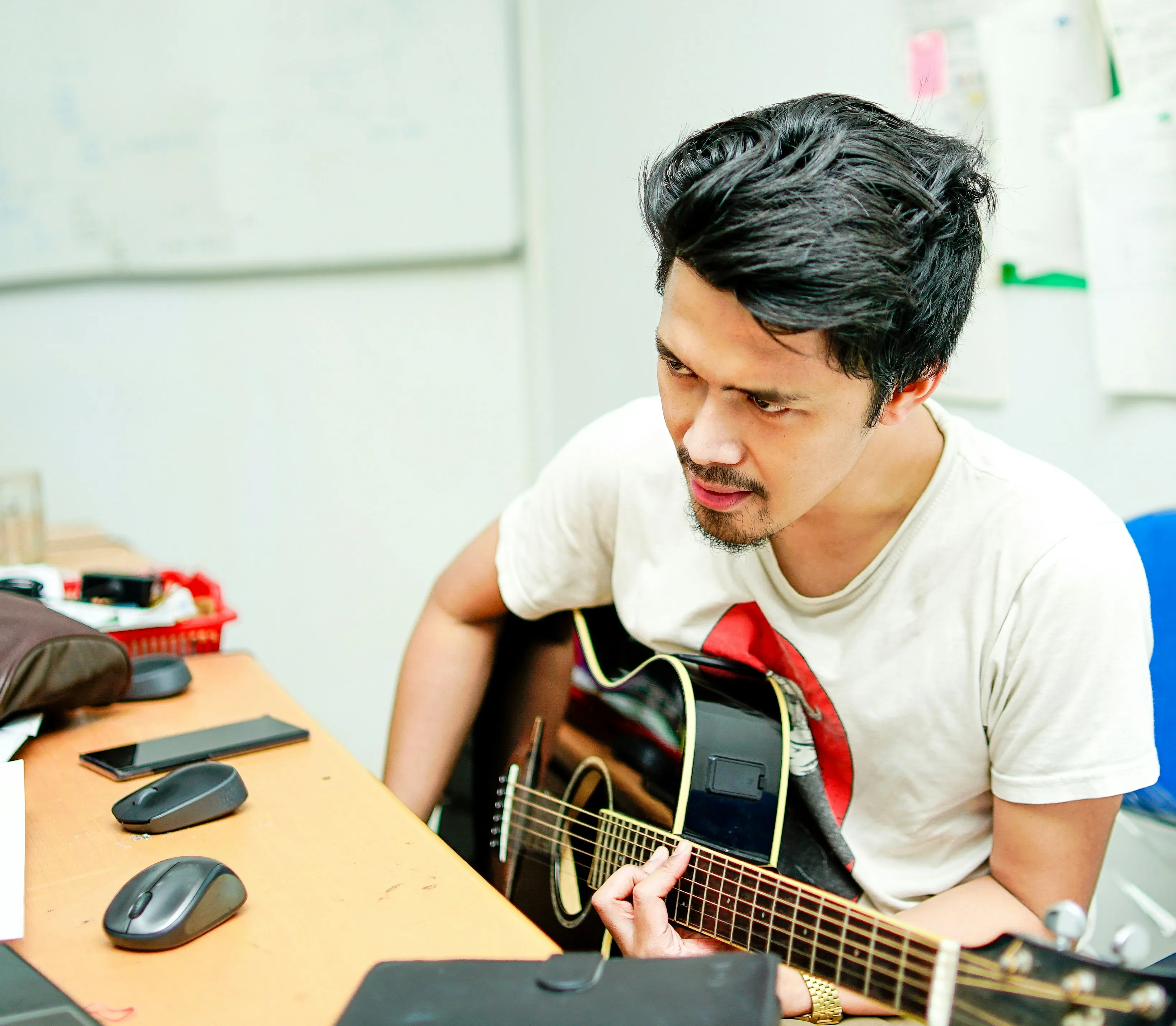 Adult guitarist focused while practicing chord transitions at a desk — targeted practice builds muscle memory