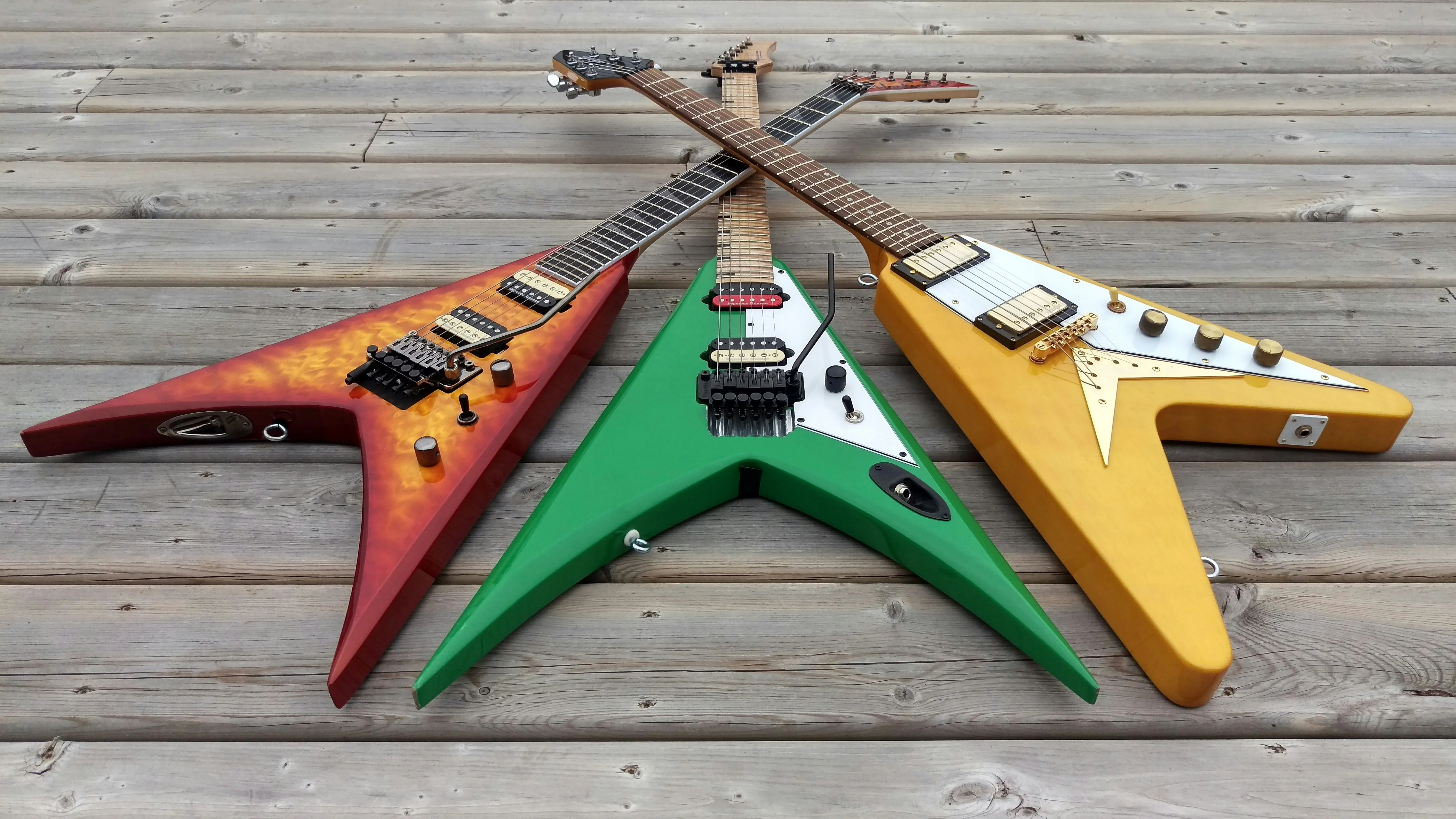 Three Flying V guitars laid out on wood — bold Gibson-style body shapes completely outside the Fender S-style legal controversy