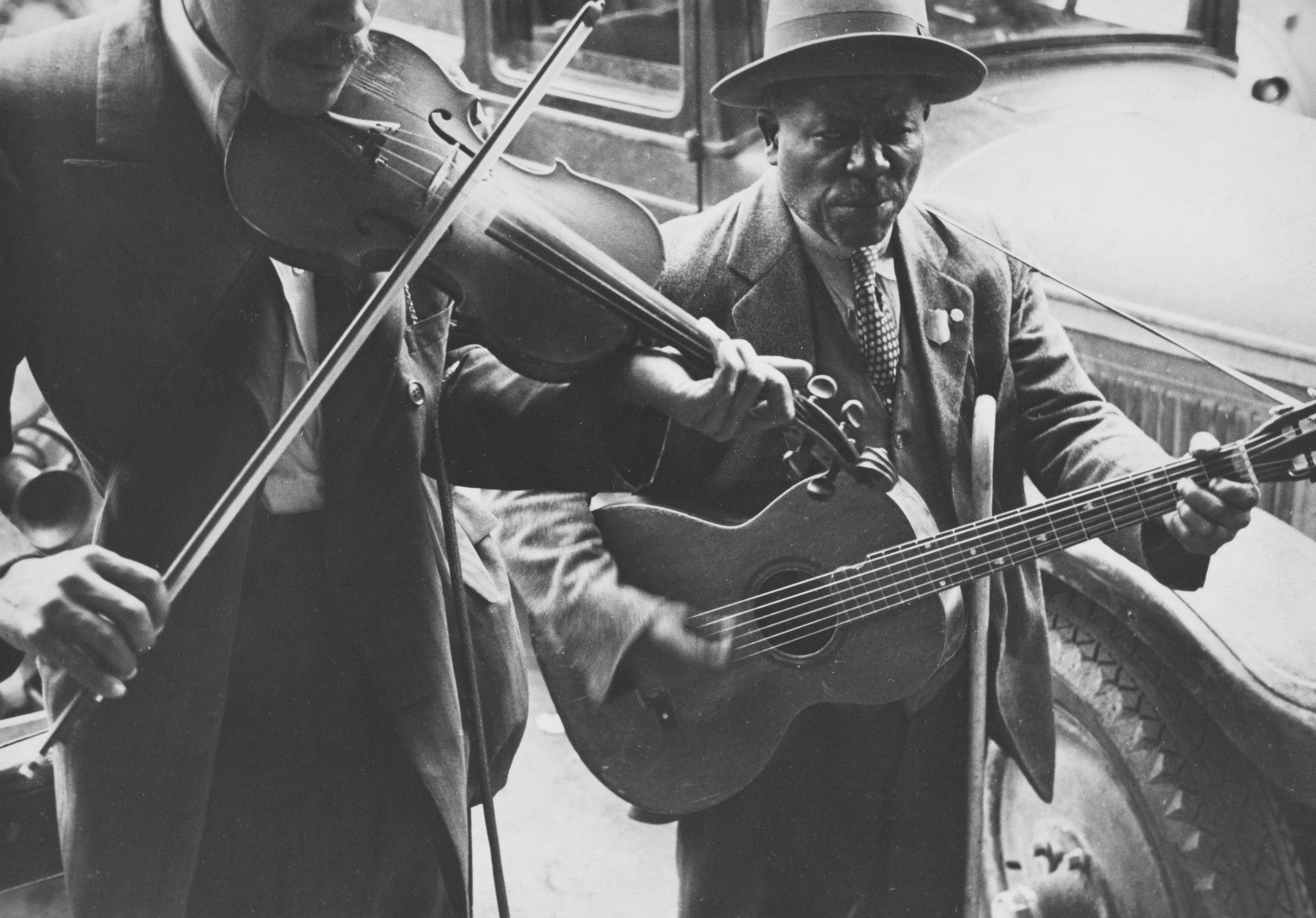 Vintage black and white photo of older musicians playing guitar and violin together — music connects across generations