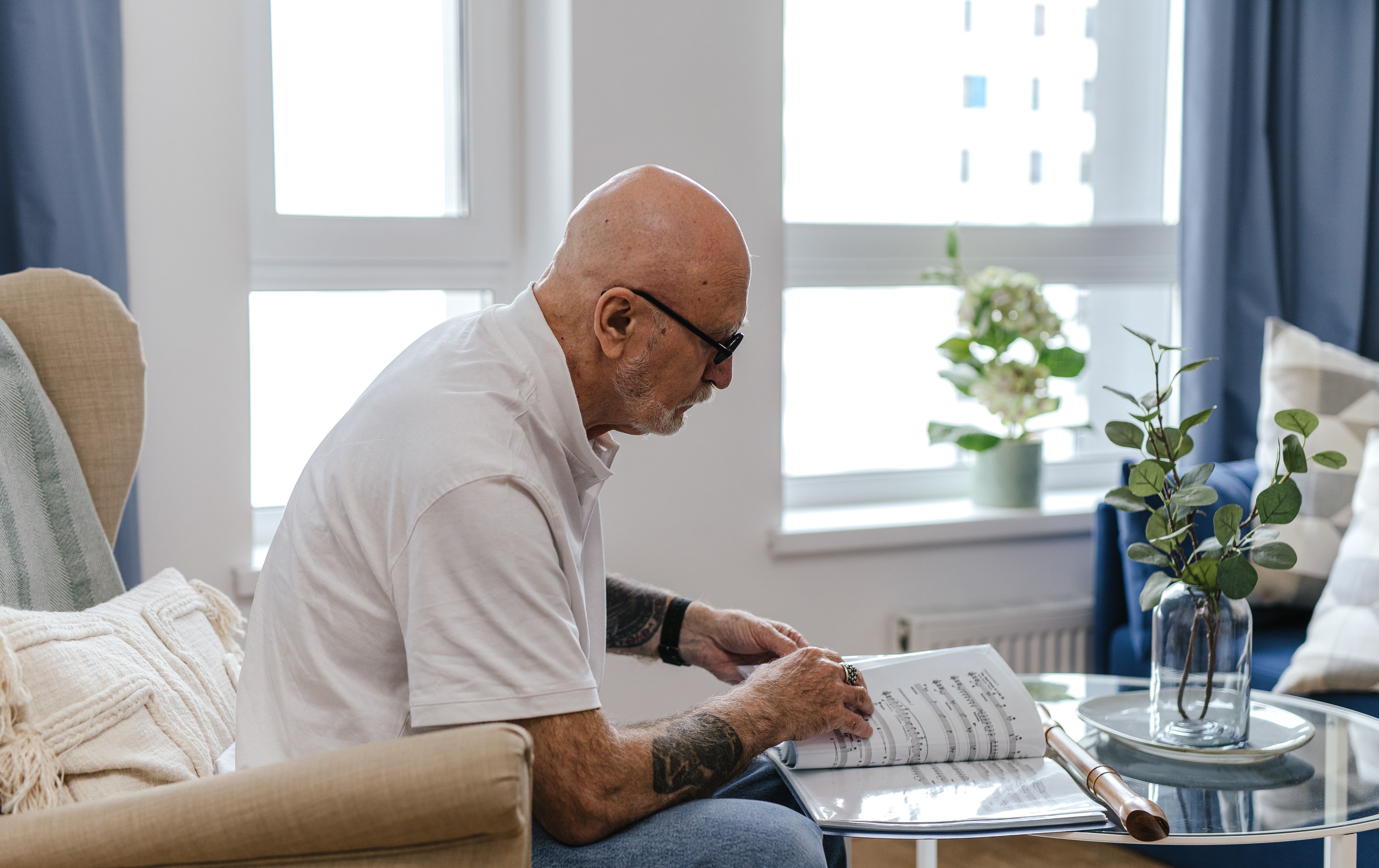 Senior man studying sheet music at home in a bright, comfortable living space — focused practice makes the difference