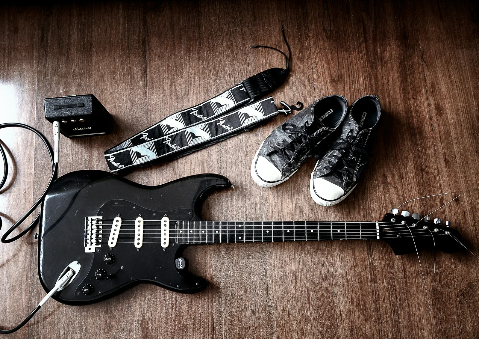 Black Stratocaster on a wood floor with Fender strap and Marshall mini amp