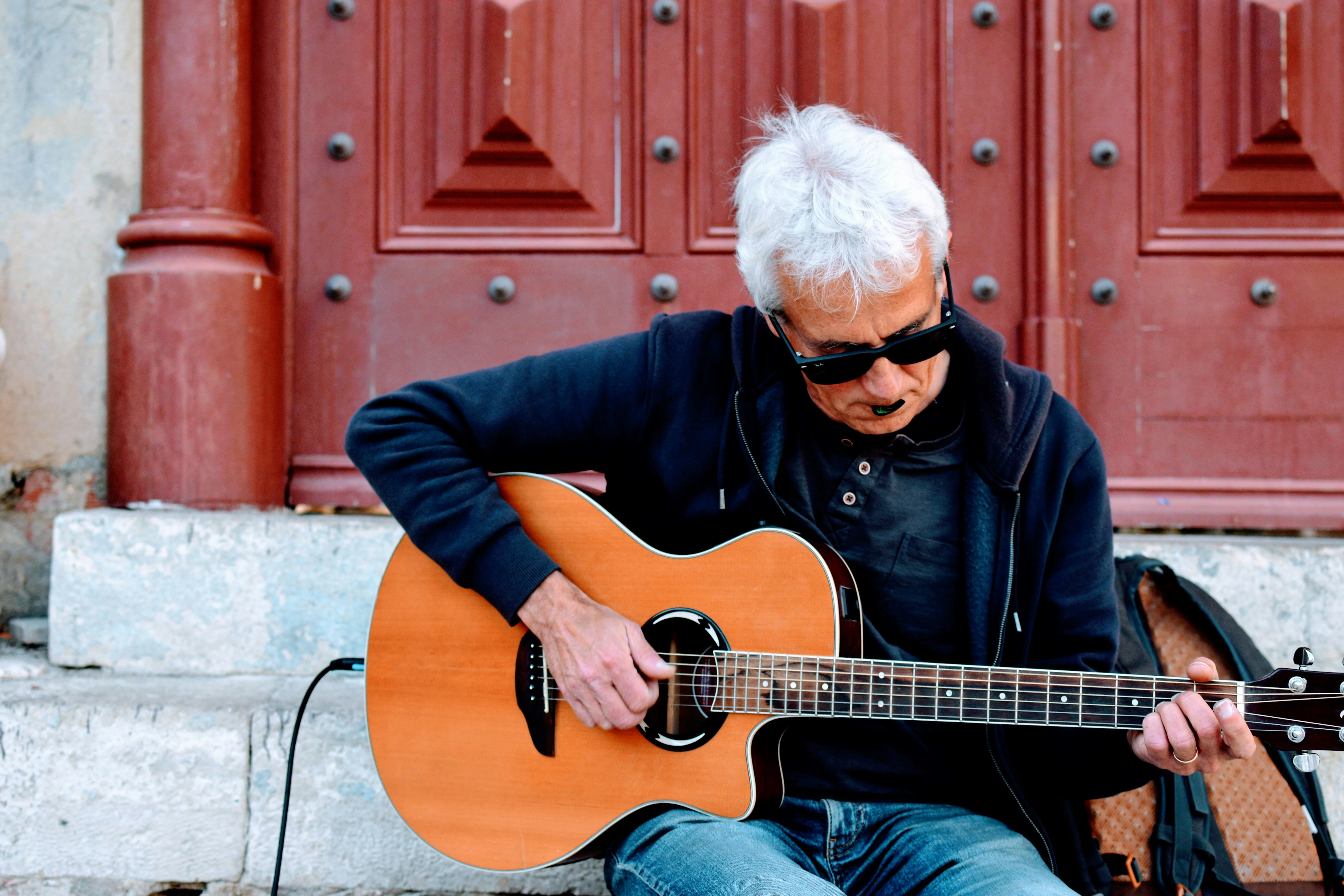 Older adult guitarist sitting on steps playing acoustic guitar — practicing alone