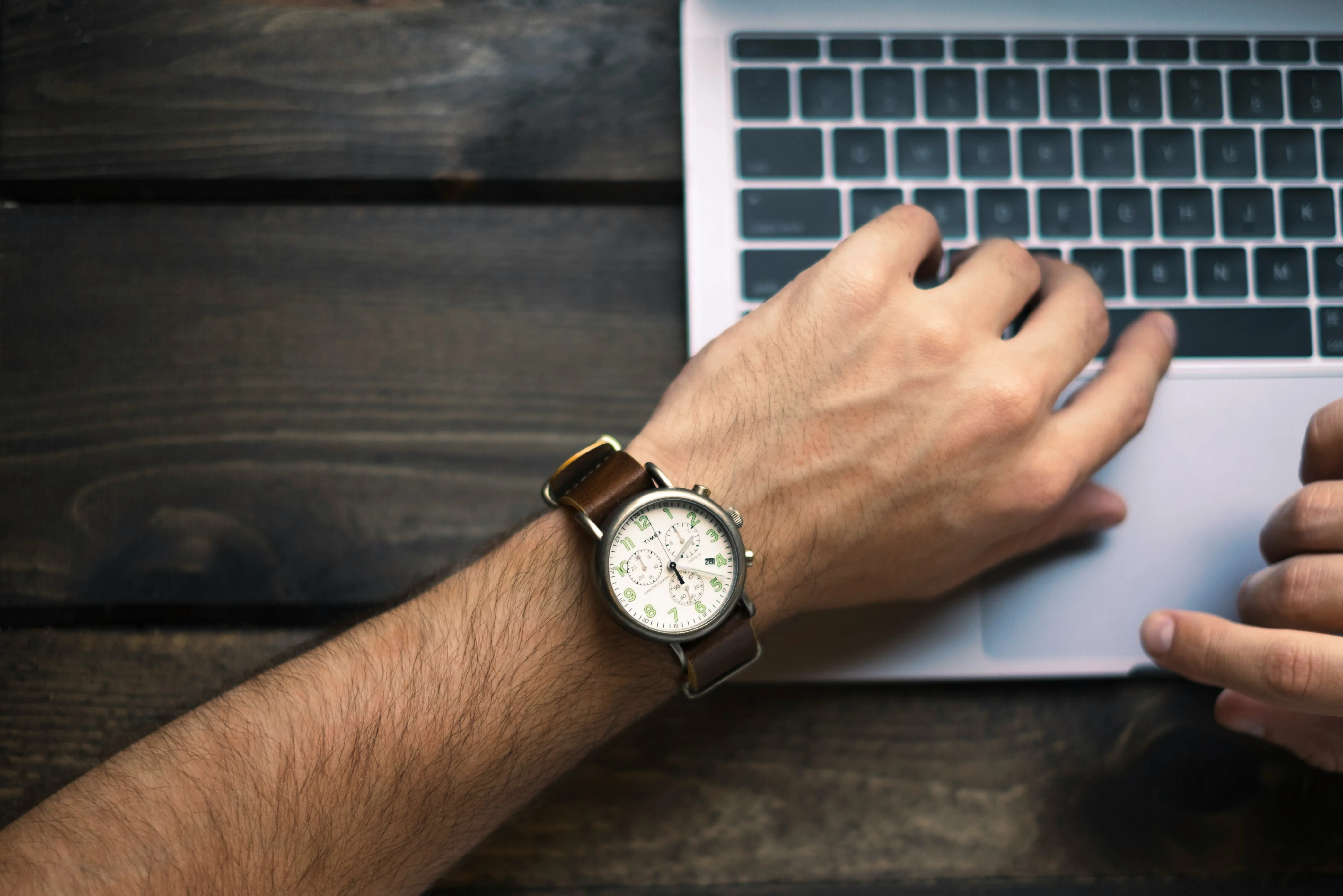 A wristwatch on someone's wrist beside a laptop keyboard during the workday — the schedule that eats into guitar practice time